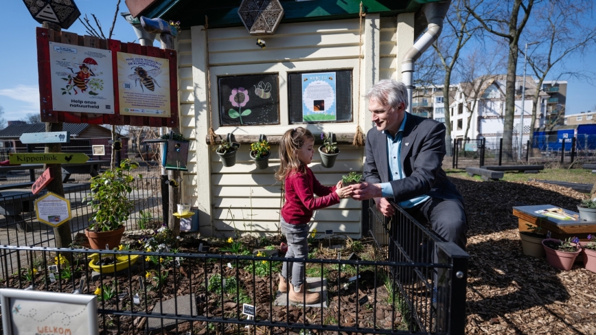 Gedeputeerde Berend Potjer geeft een plantje aan Evineva, een jonge bezoeker van stadsboerderij Molenweide, om een plantje in de grond te zetten in het bij-tanktuintje